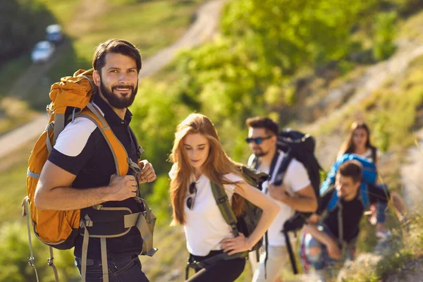 Muž batohem se svými přáteli šplhá na vrchol hory. Tým turistů horolezectví na letní dovolenou venku — Stock fotografie