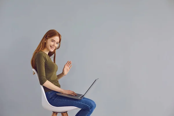 オンライン通信。グレーの背景にノートパソコンで家族や友人や同僚と話している若い女の子。スペーステキストのコピー — ストック写真