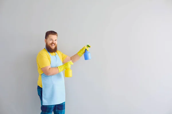Schoonmaakdienst en huishoudelijk werk concept. Happy funny guy met wasmiddelen op grijze achtergrond, ruimte voor tekst — Stockfoto