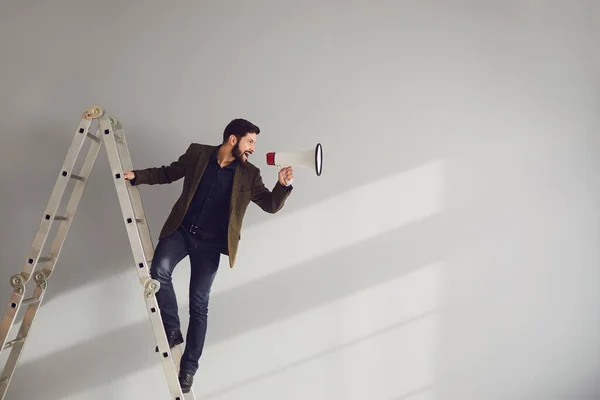 Um empresário barbudo nas escadas com um megafone na mão grita em um fundo cinza . — Fotografia de Stock