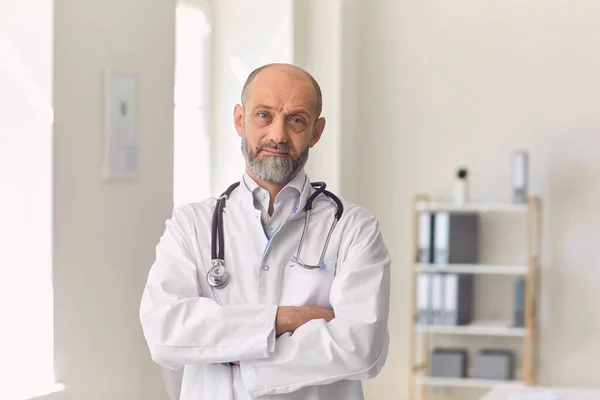 Poważny starszy lekarz w mundurze patrzący przed kamerą podczas konsultacji online z klientem w klinice — Zdjęcie stockowe