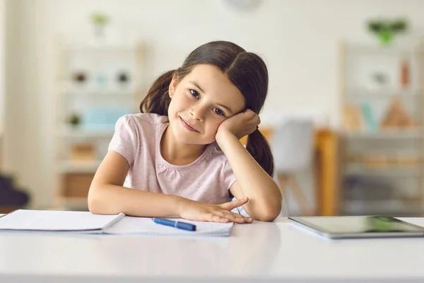 Em linha. Menina criança olha para a câmera do gadget on-line sentado atrás de uma palha na sala . — Fotografia de Stock