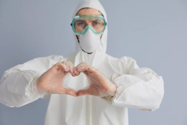 Tehlikeli madde giysisi içindeki doktor, kalbi gri arka planda gösteriyor. Sıhhiye, salgınla mücadeleye yardım için bağış yapmayı teşvik ediyor