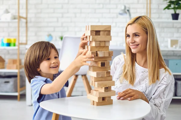 Anak kecil membangun menara dari balok kayu dengan ibu di rumah. Orangtua dan anak bermain papan permainan bersama-sama di dalam ruangan — Stok Foto