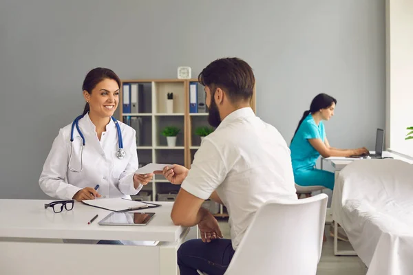 Der Arzt gibt dem Patienten ein Rezept, während er am Tisch im Büro der Klinik sitzt.. — Stockfoto