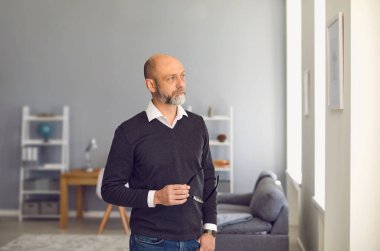 Ciddi bir adam. Gözlüklü bir bunak. Evdeki bir odada dikilirken başka tarafa bakıyor..