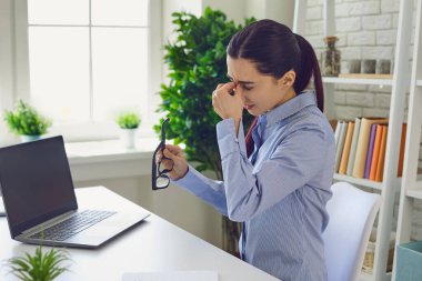 Yorgun iş kadını laptopta sıkı çalıştıktan sonra burnunu ovalıyor..