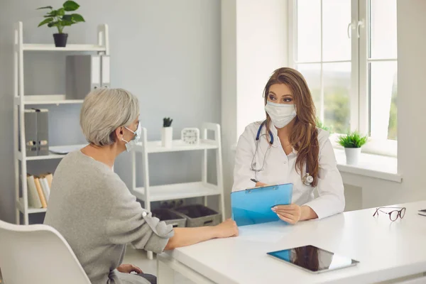 Starszy pacjent i kobieta w maskach ochronnych w klinice. Dojrzała kobieta odwiedza lekarza w celu leczenia wirusa w szpitalu — Zdjęcie stockowe
