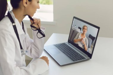 Doktor çevrimiçi danışma. Kadın doktor, yaşlı bir hastayı videolu arama bilgisayarı kullanarak dinliyor..