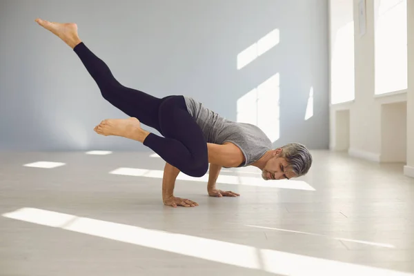 Hombre del yoga. Un hombre está practicando el equilibrio del yoga en una habitación gris. —  Fotos de Stock