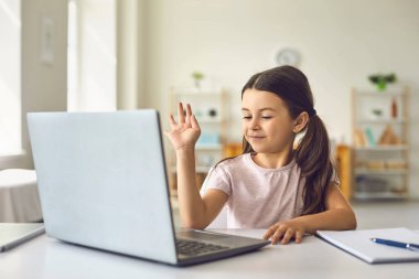 İnternette çocuk. Küçük bir kız evde bir masada otururken iletişim kurmak için bilgisayarlı görüntülü konuşma kullanıyor..
