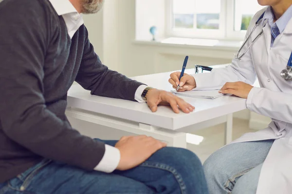 Primo piano del paziente anziano in visita dal medico presso lo studio medico. Giovane professionista che aiuta il cliente maturo in ospedale — Foto Stock