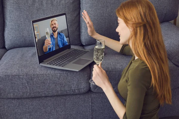 Fecha en línea citas. Una joven está en una sala de estar con un ordenador portátil. En la pantalla del portátil un joven guapo con una copa de vino. —  Fotos de Stock