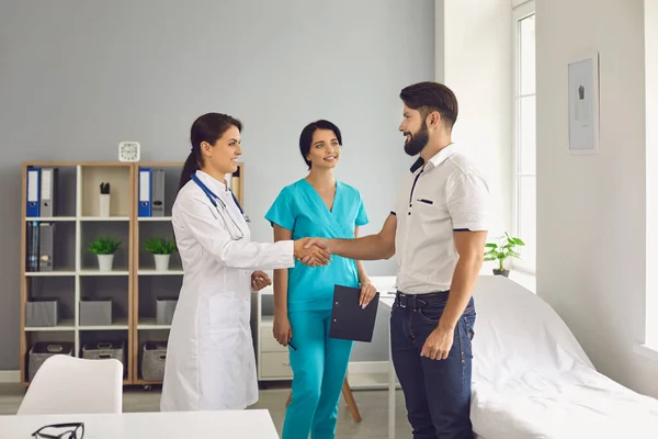 Paciente do sexo masculino feliz apertando as mãos com o jovem médico e enfermeira na clínica. Cliente grato agradecendo a ajuda da equipe médica — Fotografia de Stock