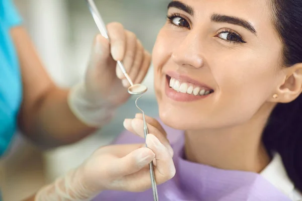 Zahnarzt mit Handschuhen in der Zahnklinik untersucht die Zähne im Mund eines lächelnden Mädchens mit Zahntechnik. — Stockfoto
