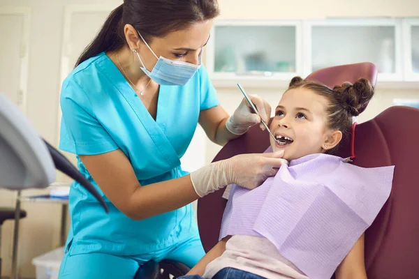 Menina em um dentista pediátrico com máscara e luvas de serviço de cuidados com os dentes da criança em uma clínica odontológica . — Fotografia de Stock