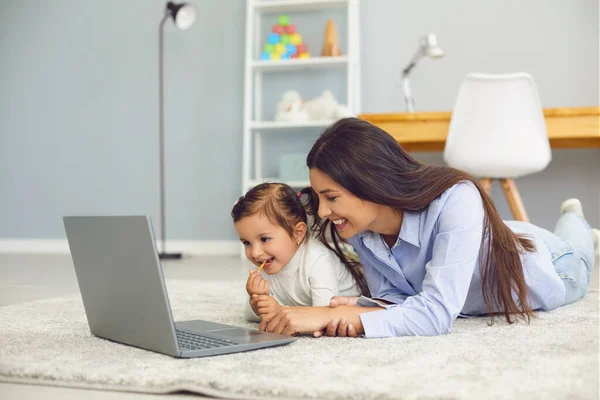 Mãe feliz e sua filhinha bonitinha assistindo vídeo de entretenimento online juntos no laptop em casa — Fotografia de Stock