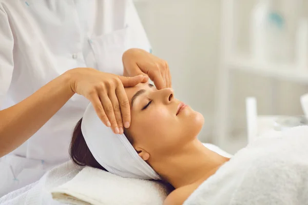 Kobiecy masaż twarzy. Profesjonalny kosmetyk wykonuje zabiegi masażu dla klienta w salonie kosmetycznym. — Zdjęcie stockowe