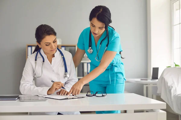 Die junge Ärztin und ihre Assistentin arbeiten im Krankenhaus zusammen. Arzt und Krankenschwester mit Dokumenten in Arztpraxis — Stockfoto