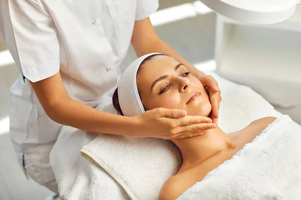 Hands of cosmetologist massaging relaxed womans face in spa beauty salon — Stock Photo, Image