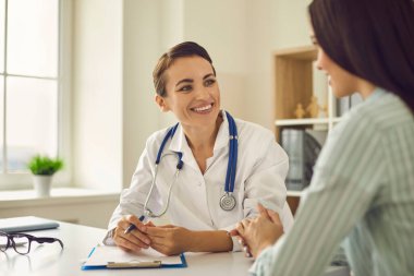 Genç doktor, klinikte hasta kadınla konuşuyor.