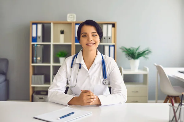 Une médecin femme en manteau blanc regarde dans la caméra d'un ordinateur portable et consulte un patient à l'aide d'une application de clinique d'appel vidéo. — Photo