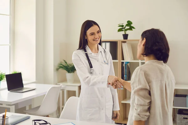 Friendly female doctor shaking hands with patient at hospital. Young medic greeting client at medical office — Stock Photo, Image