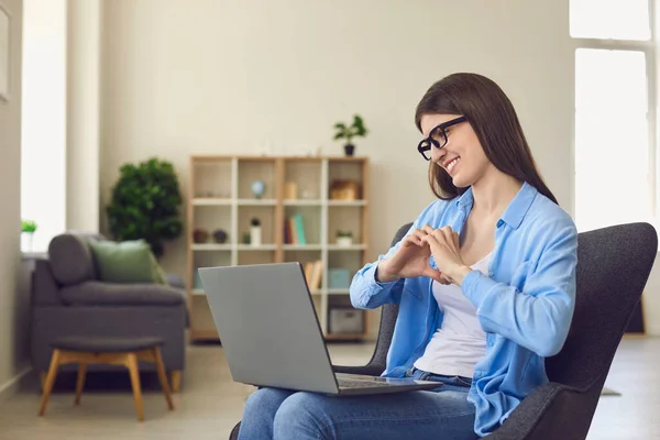 Online-Dating. Glückliche junge Frau im Gespräch mit ihrem Freund auf dem Laptop. Liebendes Mädchen zeigt Herz mit Händen auf PC-Bildschirm — Stockfoto