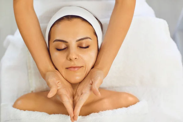 Mujer joven recibiendo masaje facial en el salón kosmetogicheskom. Cuidado facial de la piel. — Foto de Stock