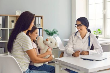 Aile doktoru. Tıp doktoru kadın, kliniğin ofisinde oturan anne ve çocuğa danışıyor..