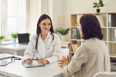 Genç, gülümseyen doktor terapisti hastaları dinliyor ve klinikte notlar alıyor.