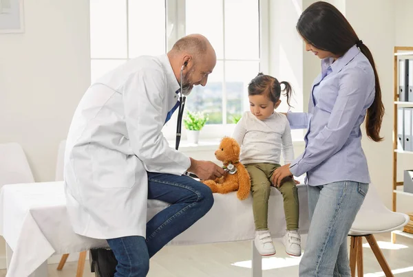 Starší lékař se stetoskopem poslouchá malou holčičku s matkami v nemocnici. — Stock fotografie