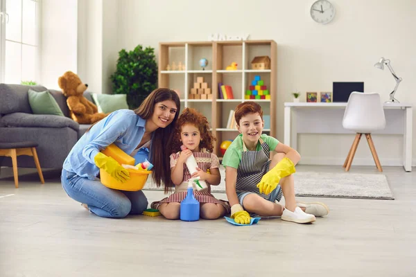 Szczęśliwa matka i dzieci w rękawiczkach domowych siedzących na podłodze i patrzących w kamerę — Zdjęcie stockowe