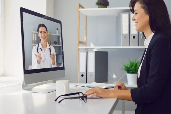Fiatal gyönyörű üzletasszony van az irodában a munkahelyen használ egy videohívást, hogy beszéljen egy orvos az interneten. — Stock Fotó