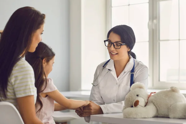 Aile hastalarına klinikte pratisyen hekim danışır. Kadın doktor kıza gülümsüyor ve annesi ofiste masada oturuyor.. — Stok fotoğraf