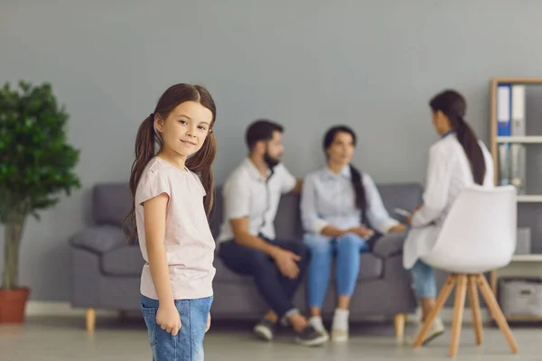 微笑的女孩站在诊所里，面对着与女医生交谈的父母 — 图库照片