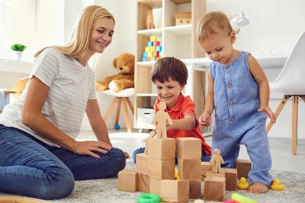 Mam en zoon bouwen een toren van houten kubussen in de kamer. Moeder geeft op de vrije dag thuis les aan kinderen — Stockfoto