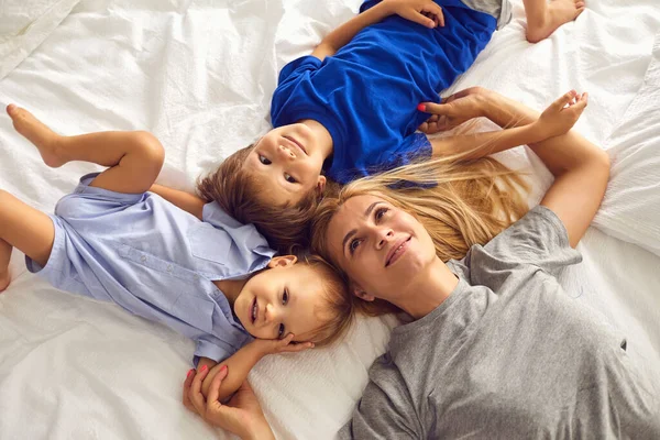 Madre e hijos están acostados sonriendo abrazándose en la cama de la habitación. Día de las Madres. — Foto de Stock