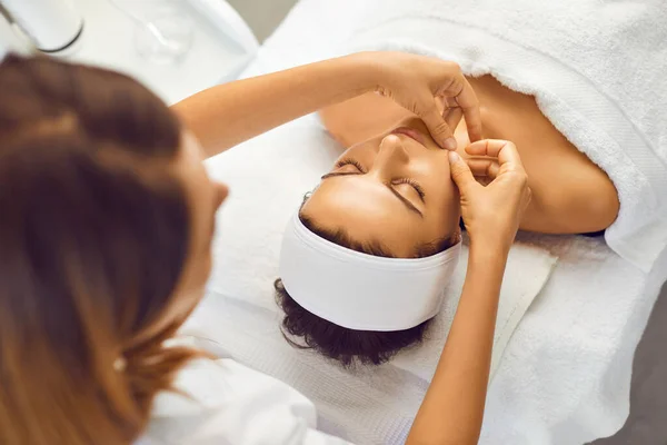 Cosmetologist making facial massage for serene young woman in beauty salon — Stock Photo, Image