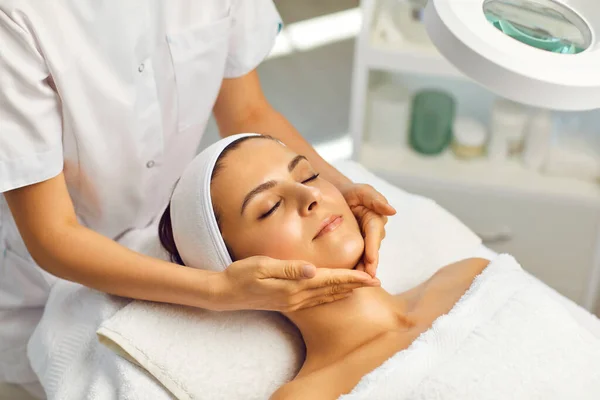 Cosmetologo fare trattamento di massaggio di bellezza del viso per la giovane donna nel salone di bellezza termale — Foto Stock