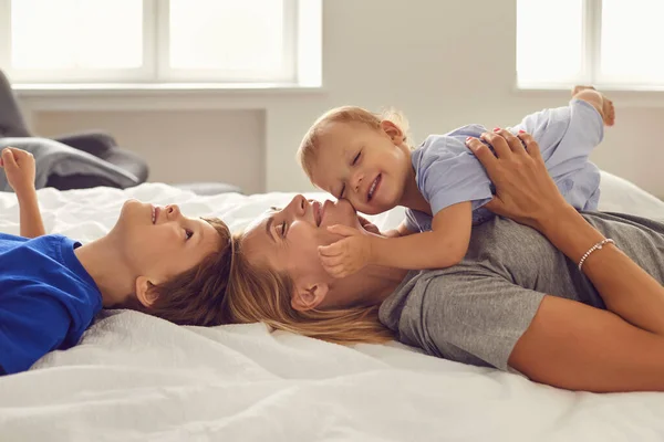 Ibu dan anak-anak berbaring tersenyum sambil memeluk di tempat tidur di kamar. Hari Ibu. — Stok Foto