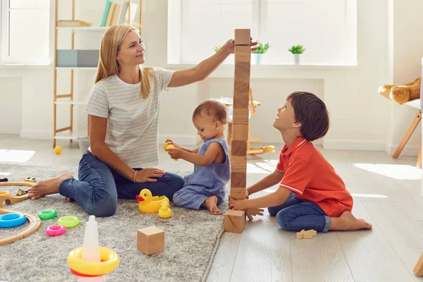 Ibu dan anak-anak sedang membangun menara batu kayu di dalam ruangan. Ibu mengajar anak-anak pada hari libur di rumah. — Stok Foto