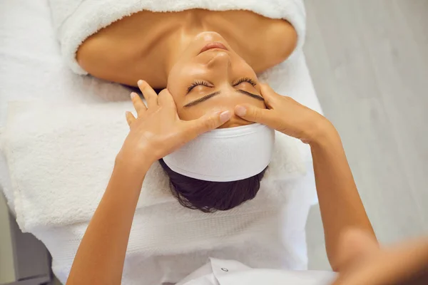 Manos del cosmetólogo haciendo masaje de belleza facial para relajar a la mujer joven, vista trasera —  Fotos de Stock