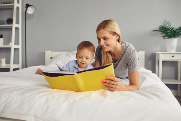 Ibu dan anak membaca buku saat berbaring di tempat tidur di kamar. Hari Ibu. — Stok Foto