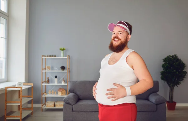 Uomo grasso divertente in pantaloncini rossi e t-shirt bianca sorridente facendo esercizi nella stanza — Foto Stock