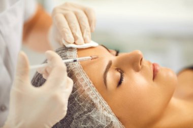 Kozmetik uzmanı güzellik salonundaki genç bayana yüz güzelliği iğnesi yapıyor.