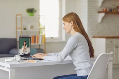 Online eğitim. Evdeki masada oturan genç kız online ders için dizüstü bilgisayar kullanıyor. Üniversitede, okulda uzaktan öğrenim.