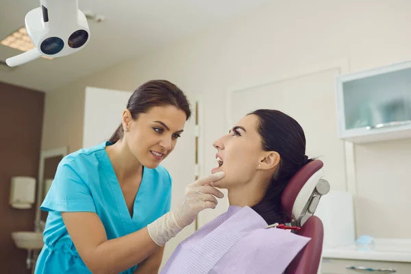 Zahnärztin betrachtet offenen Patientinnenmund und untersucht ihre Zähne in Zahnklinik — Stockfoto