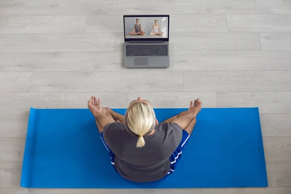 Yoga en línea en casa. Hombre joven siguiendo clases de yoga en línea y haciendo su meditación matutina o ejercicios de respiración en la esterilla en casa — Foto de Stock