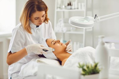 Genç kozmetolog ya da dermatolog güzellik salonundaki kadın için ultrason yüz temizliği yapıyor.